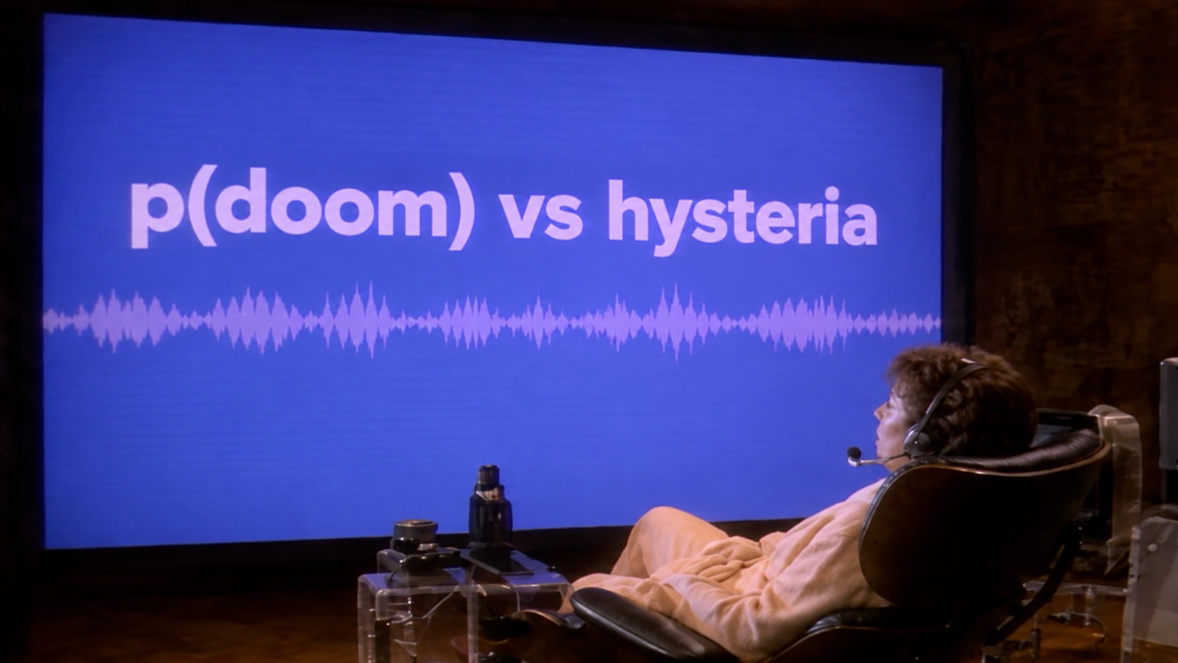 A person reclines in a headset before a wall-sized screen reading “p(doom) vs hysteria” above an audio waveform